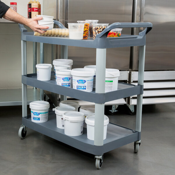 A man using a Rubbermaid Xtra three shelf utility cart to hold food items.
