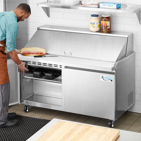 A man in an apron using an Avantco stainless steel commercial sandwich prep refrigerator.