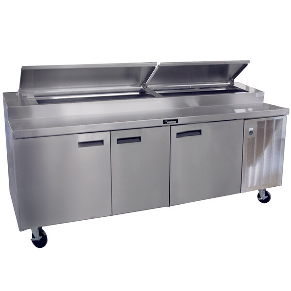 A Delfield stainless steel pizza prep table with three doors on a counter in a large commercial kitchen.