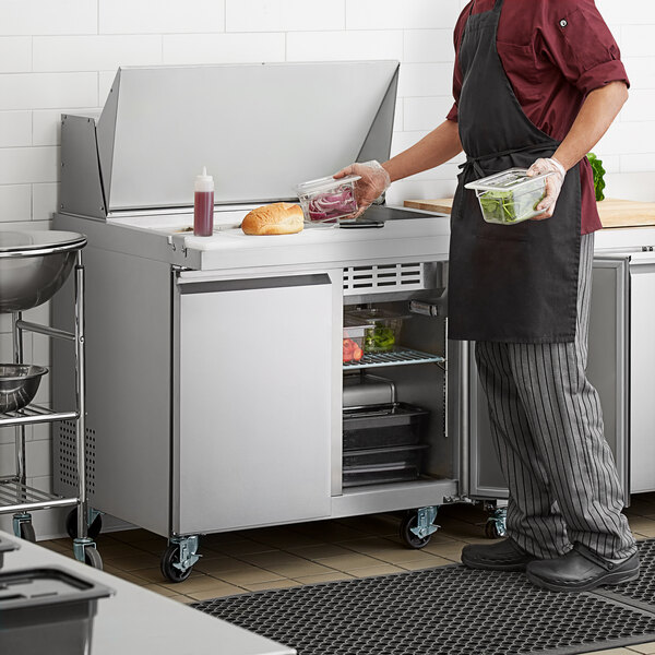 An Avantco stainless steel sandwich prep table in a professional kitchen with a man putting food into it.
