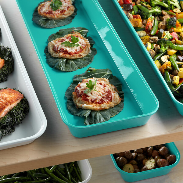 A green Cambro market pan on a table filled with food and vegetables.