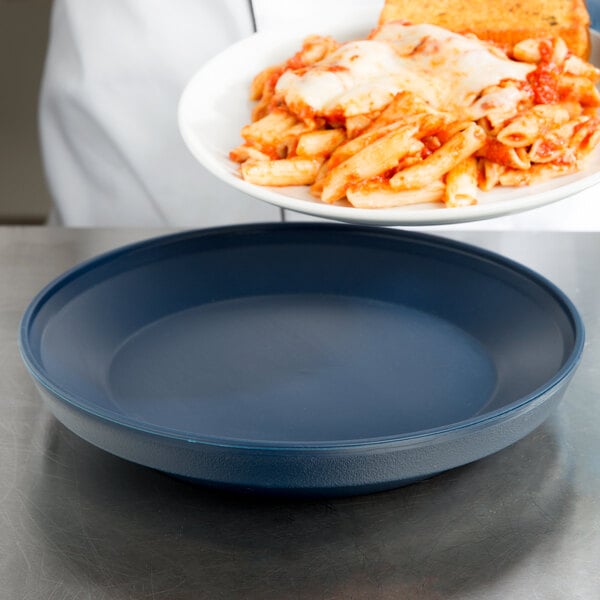 A person holding a plate of pasta with cheese and sauce on a Dinex Dark Blue insulated meal delivery base.