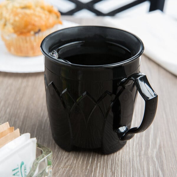 A black Dinex insulated mug with a handle on a table with a muffin.
