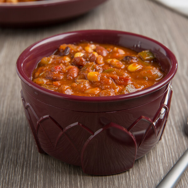 A Dinex cranberry insulated bowl filled with chili topped with beans and vegetables on a wood surface.