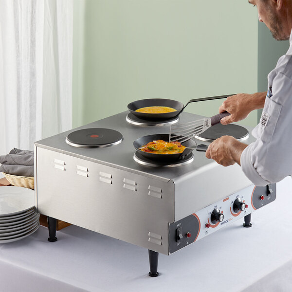 A man cooking food on a Nemco countertop raised hot plate with solid burners.