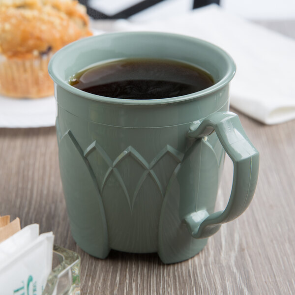A Dinex sage insulated mug of coffee on a table next to a muffin.