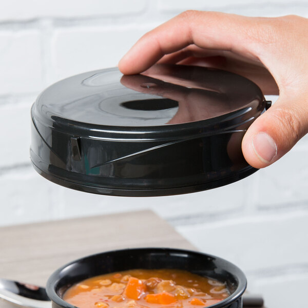 A hand holding a black Dinex soup bowl lid over a bowl of soup.