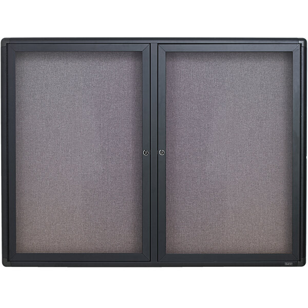A Quartet graphite aluminum enclosed fabric cork bulletin board with two black framed glass doors.