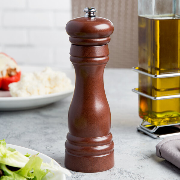 A Fletchers' Mill walnut-stained pepper mill on a table next to a plate of salad.