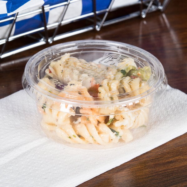 A clear Fabri-Kal plastic souffle lid on a plastic container of pasta on a napkin.