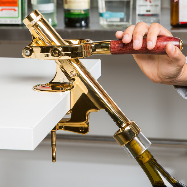 A person using a Franmara gold-plated counter mount wine bottle opener to open a bottle of wine.
