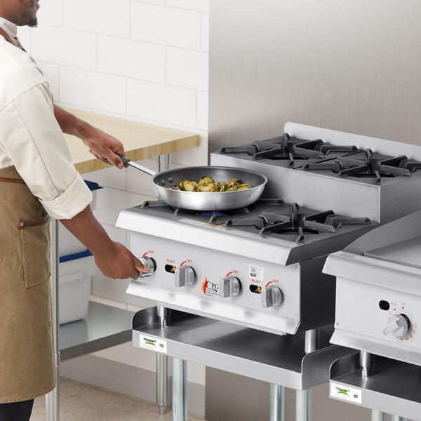 A man cooking food on a Cooking Performance Group countertop range with four burners.