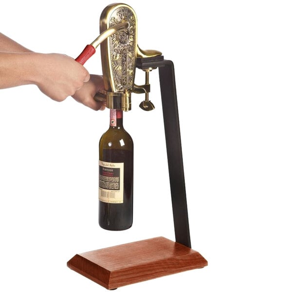 A person using a Franmara brass-plated wine bottle opener on a table stand to open a bottle of wine.