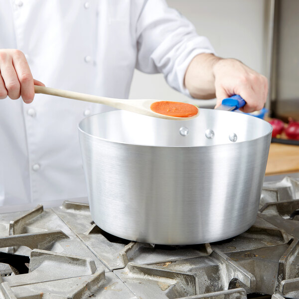 A person using a Vollrath Wear-Ever sauce pan with a wooden spoon.