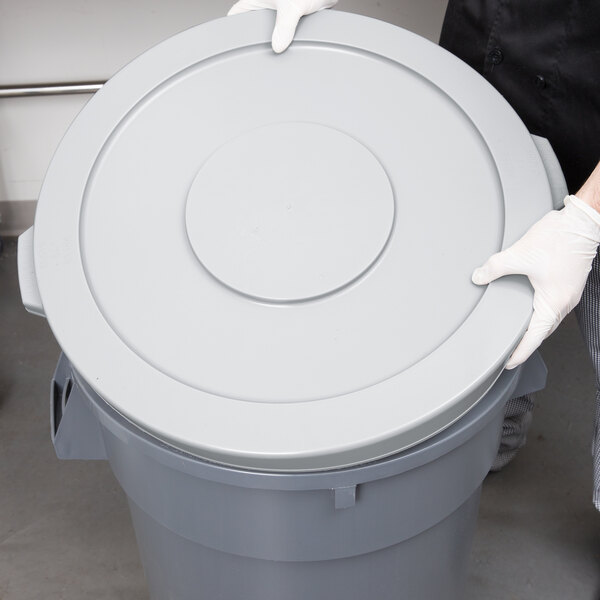 A person wearing white gloves holds a gray Continental trash can lid.