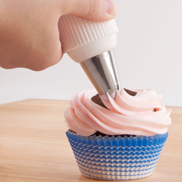 A hand using a white pastry bag with a white and pink Ateco closed star tip to frost a cupcake.