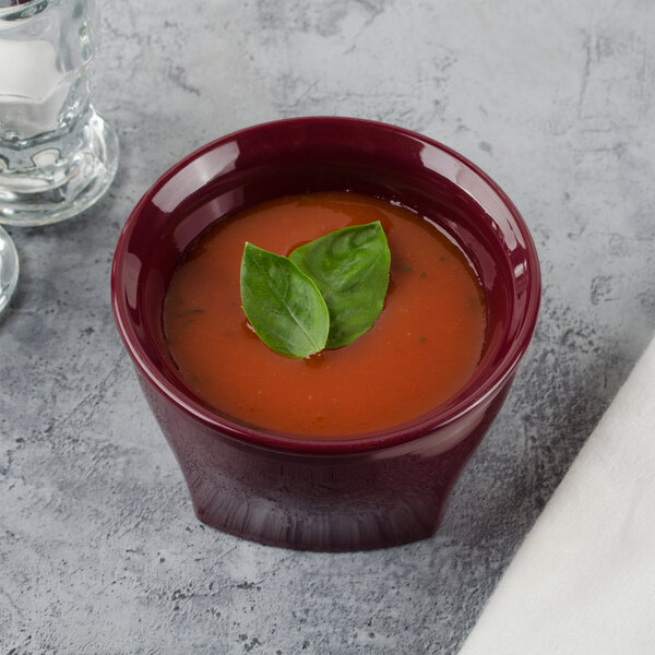 A Cambro cranberry insulated plastic bowl filled with tomato soup and topped with basil leaves.