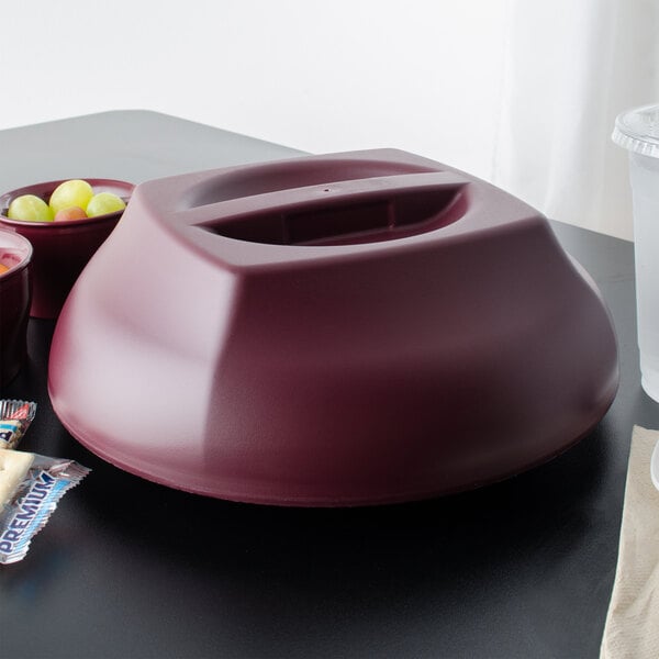 A red Cambro insulated plastic dome plate cover over a bowl of fruit.