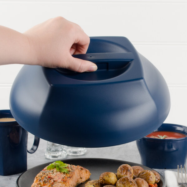 A hand holding a Cambro navy blue insulated dome plate cover over a plate of food.
