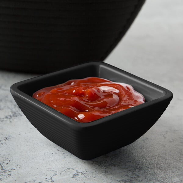 A Tablecraft black square ribbed ramekin filled with ketchup.
