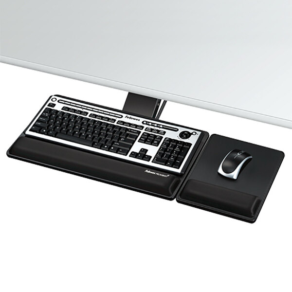 A black keyboard and mouse on a white desk with a Fellowes black keyboard tray underneath.