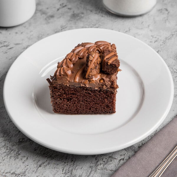 A piece of chocolate cake with frosting on a Libbey Porcelana white porcelain plate.