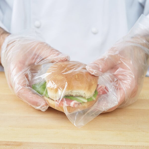 A person holding a sandwich wrapped in a plastic bag.