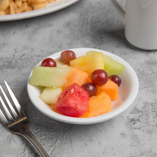 A Libbey white porcelain bowl filled with fruit with a fork next to it.