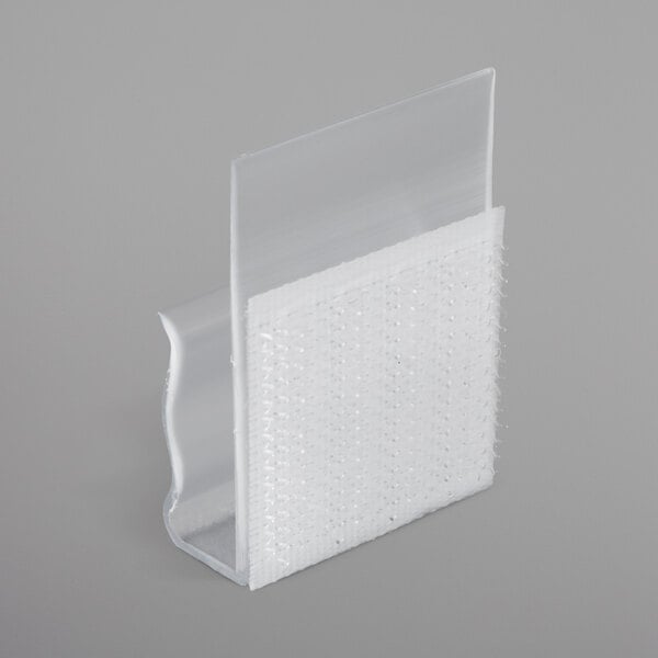 A close-up of a white plastic table skirt clip with a clear plastic strip and white hook.