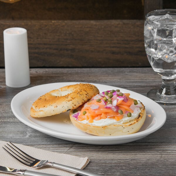 A Libbey narrow rim oval porcelain platter with a bagel with cream cheese, onions, and vegetables on it.