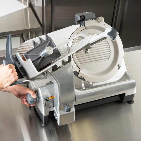 A person using a Hobart meat slicer on a counter.