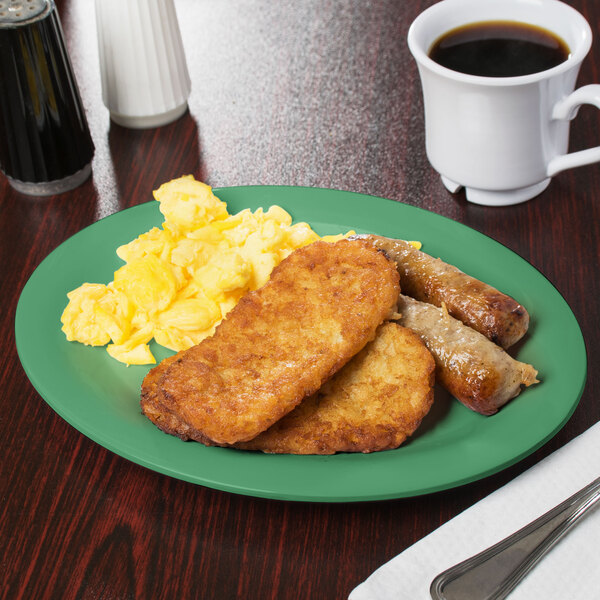 A rainforest green oval melamine platter with food including scrambled eggs, sausage, and toast on a table with a cup of coffee.