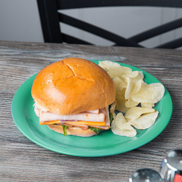 A sandwich and chips on a rainforest green narrow rim melamine plate.