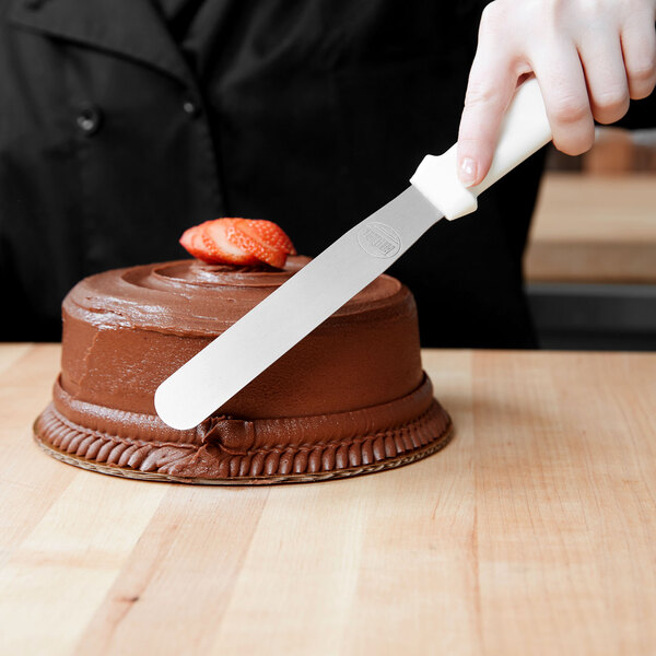 A person using a Tablecraft baking spatula to cut a chocolate cake.