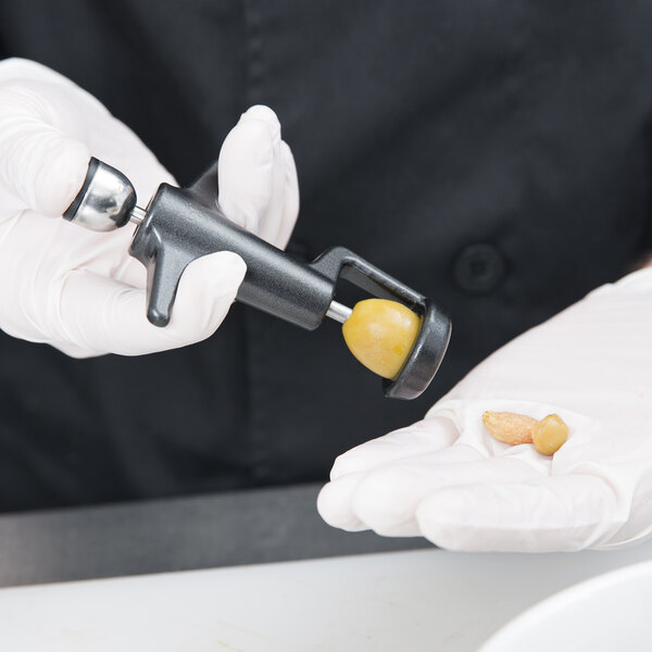 A person in gloves using a Tellier manual olive/cherry pitter to pit a nut.
