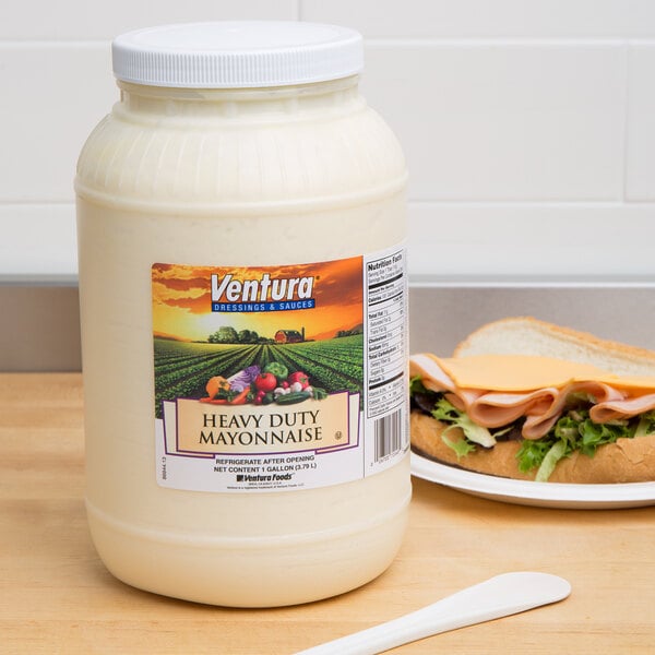 A white container of Heavy Duty Mayonnaise on a table near a sandwich with meat and lettuce.