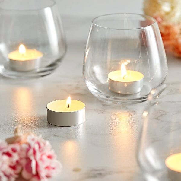 Three Leola white tea light candles in glass holders on a table with flowers.