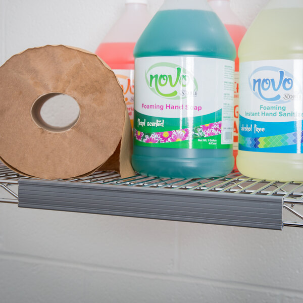 A Metro gray plastic label holder on a shelf holding bottles of hand soap and a roll of toilet paper.