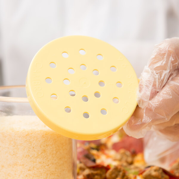 A person holding a container with a yellow Cambro cheese shaker lid over food.