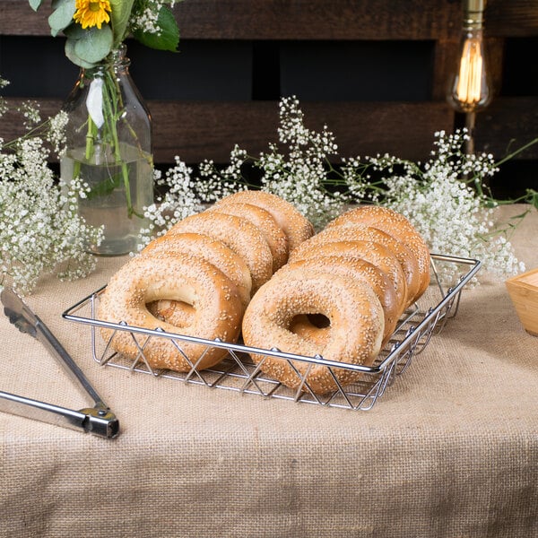 A Clipper Mill square wire basket filled with bagels with sesame seeds.