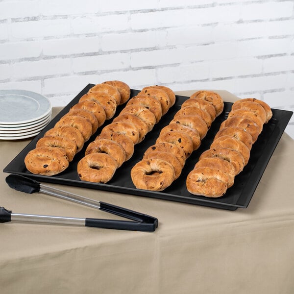 A black Siciliano square display platter with a tray of bagels on a table.