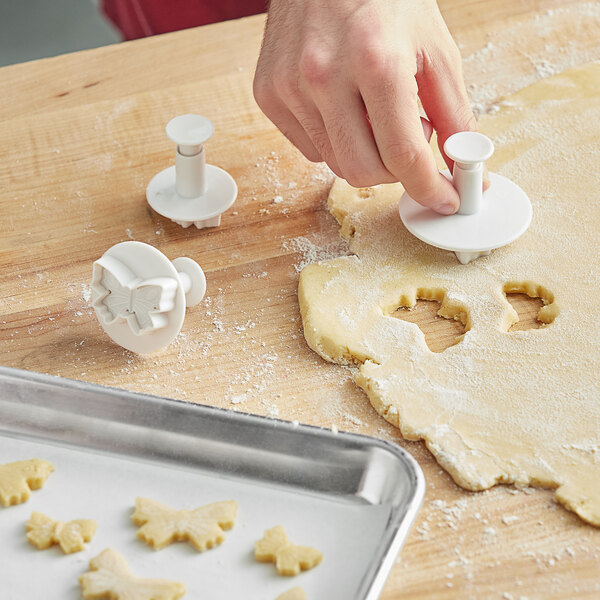 A hand using Ateco butterfly cookie cutters to cut out cookies.