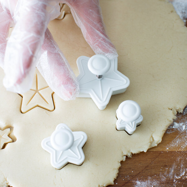 A person wearing gloves uses an Ateco plastic star plunger cutter to make star-shaped cookies.