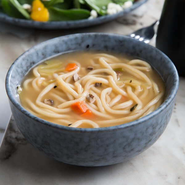 A Biseki blue stoneware bowl filled with noodle soup with vegetables.