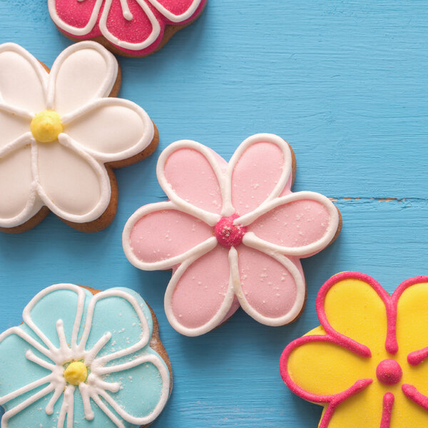 A group of flower-shaped cookies with pink and white frosting.