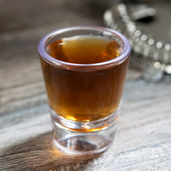 A GET SAN plastic shot glass filled with brown liquid on a table.