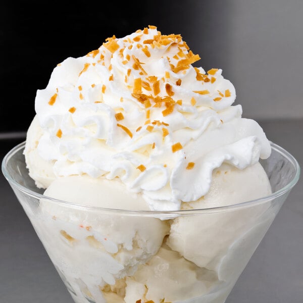 A glass bowl of ice cream topped with whipped cream and Sweet Toasted Coconut Flakes.