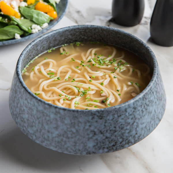 A blue stoneware bowl of soup with noodles and green onions.
