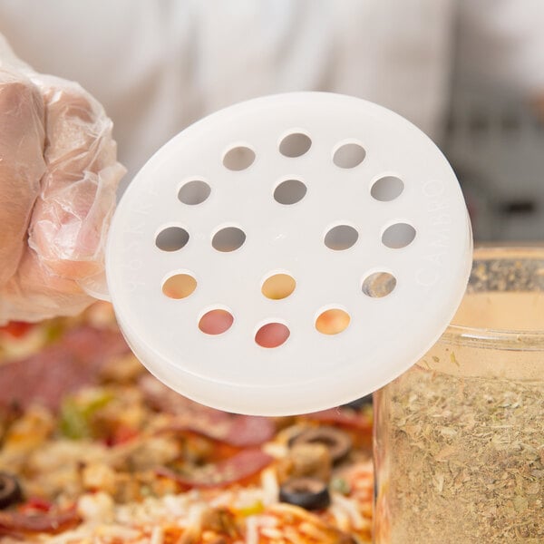 A person holding a white Cambro shaker lid with holes over a pizza.