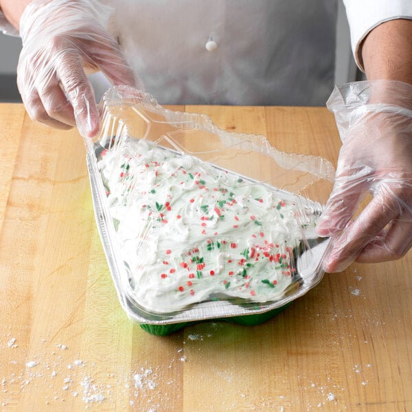 A person in gloves holding a Durable Packaging Christmas tree shaped foil bake pan filled with cake and sprinkles.